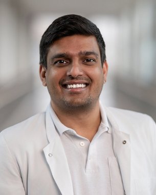 Ein lächelnder Arzt in einem weißen Kittel steht in einem hellen Flur.