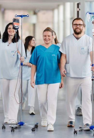 Vier Pflegekräfte in blauen und weißen Uniformen gehen gemeinsam einen Flur entlang, während sie Infusionsständer mit sich führen.